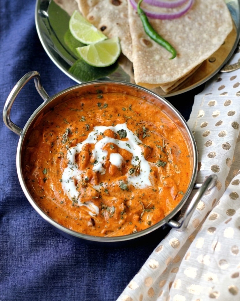 Butter chicken in a karahi with roti, lime and onion