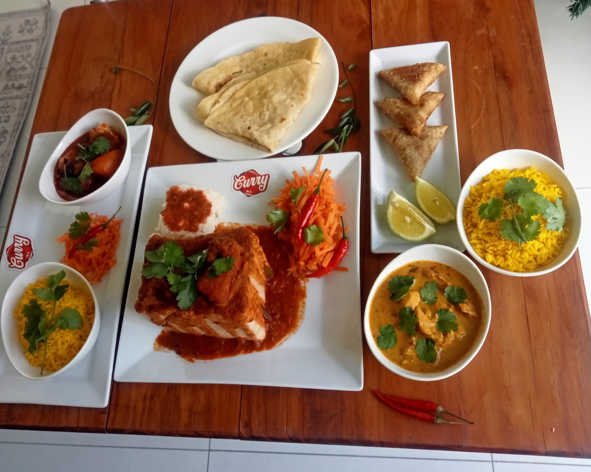 Catering spread of curries, roti, samoosas, yellow rice and carrot salad